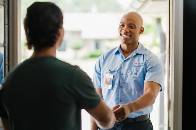 Aire Serv technician explaining air conditioning unit to woman outside of home.
