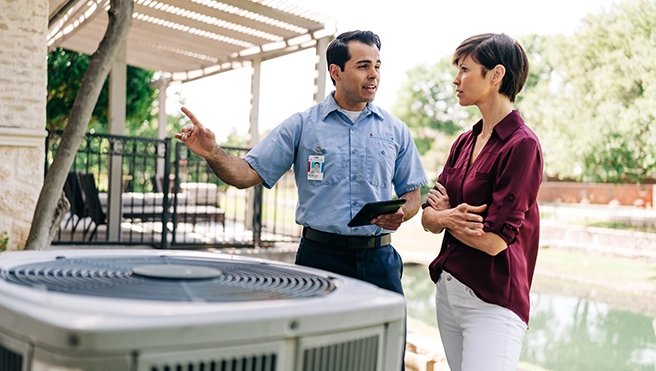 Aire Serv technician explaining air conditioning unit to woman outside of home.