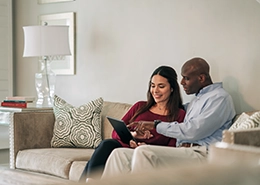 A couple sitting on a couch and looking at a tablet together.