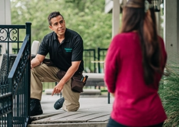A Housemaster inspector kneeling on a porch and talking to a woman standing nearby.