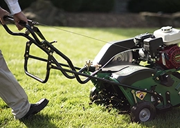 A person operating a lawn aerator machine on a grassy yard.