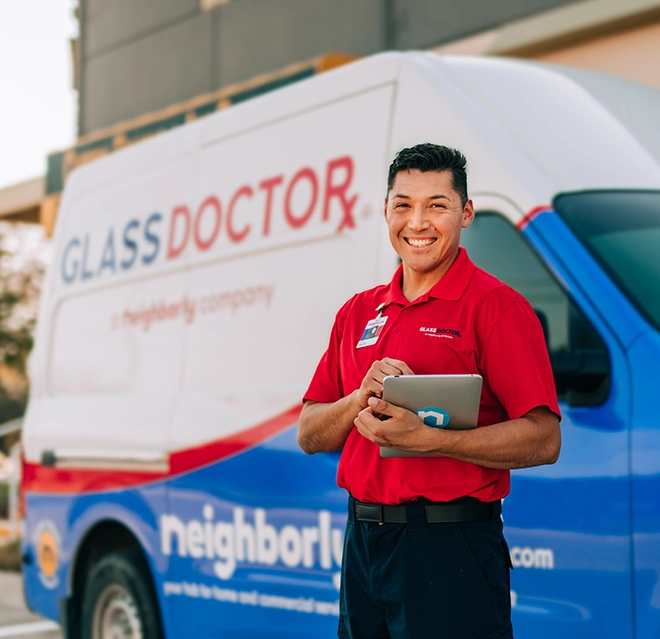 Glass Doctor technician standing standing beside a service van while using a tablet.