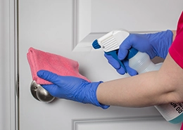 Person wearing blue gloves cleaning a doorknob.