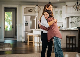 Two women hugging in home.