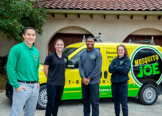 Four employees of Mosquito Joe stand smiling in front of a company van.
