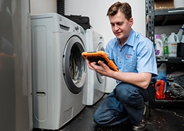 Mr. Appliance technician sitting beside a washing machine.