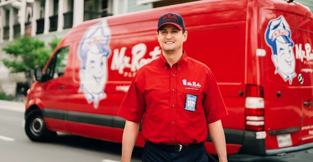 Mr. Rooter plumber standing beside a service van.