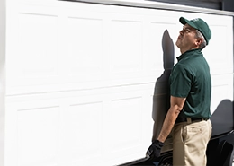 A technician in a green uniform and cap adjusts a white garage door.