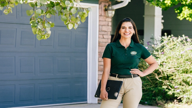 A female PDS worker smiling in front of a house.