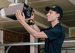 A person installs a garage door opener, using a power drill.