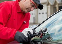 A technician repairing a car windshield using specialized tools.