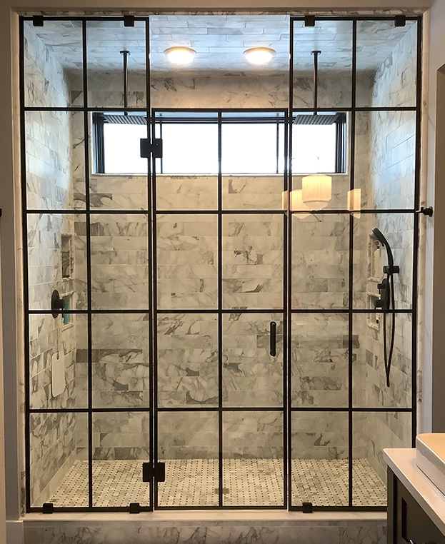 Modern shower enclosure with black metal framing, marble tile walls, and a mosaic floor.