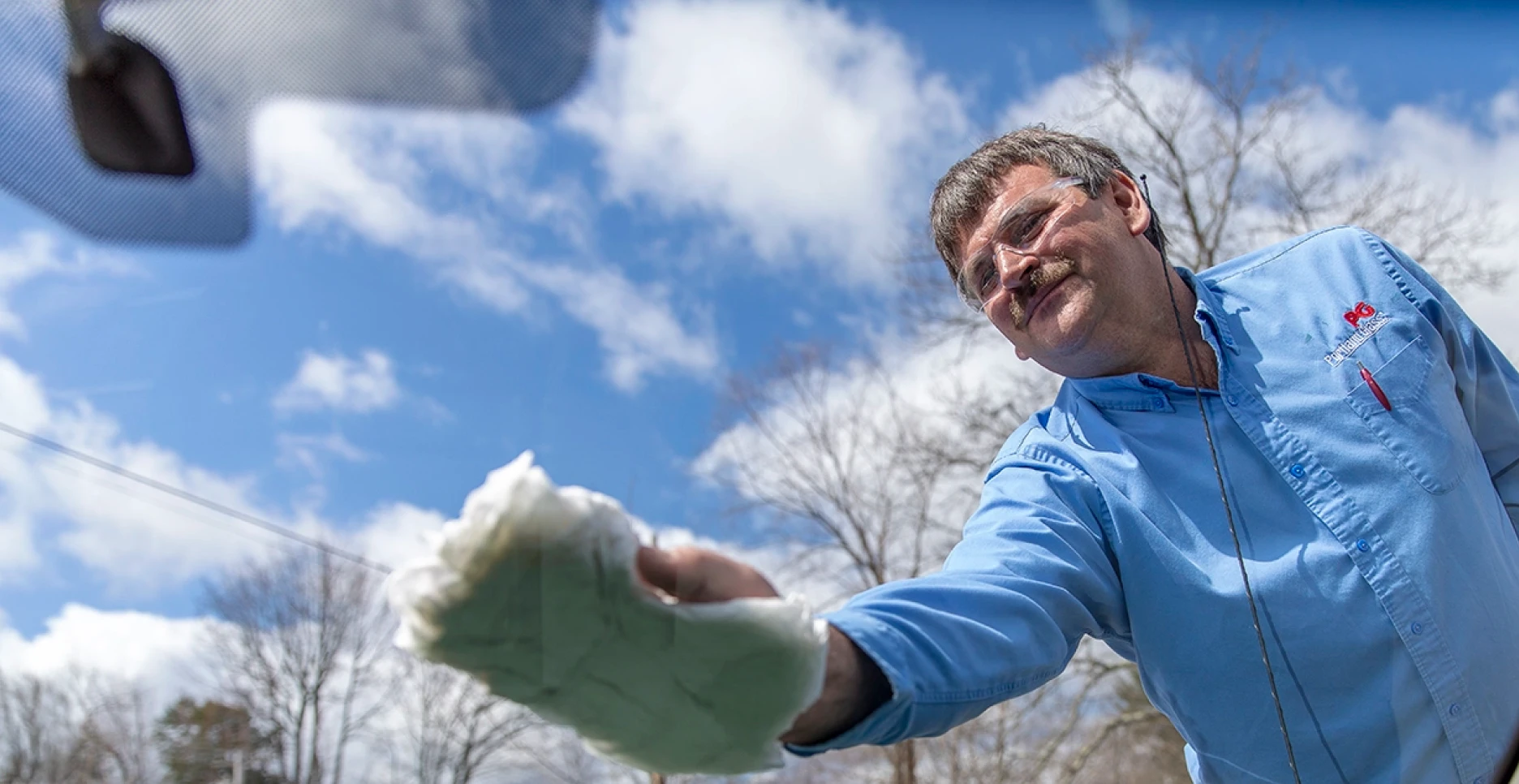 A worker cleaning a windshield with a cloth.