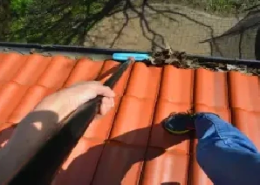 A worker removing debris from a house gutter.