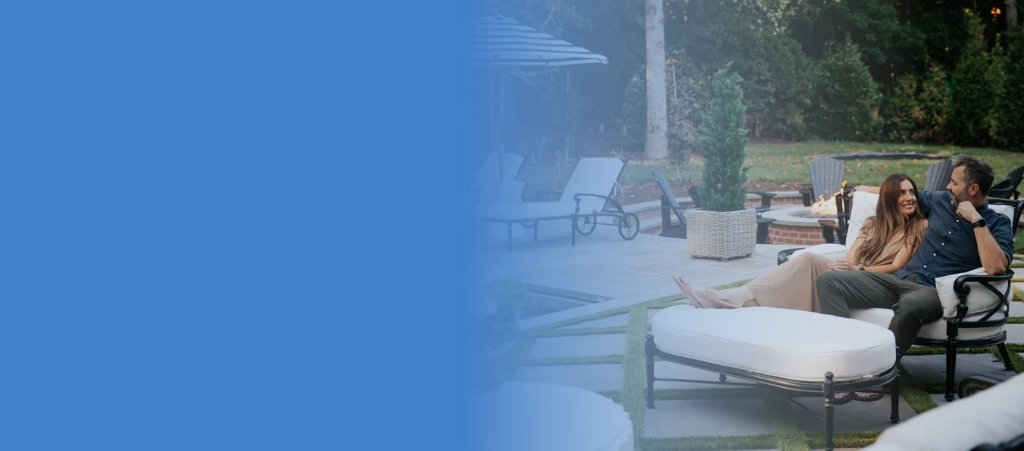 Man with arm wrapped around woman sitting outside on deck chairs.