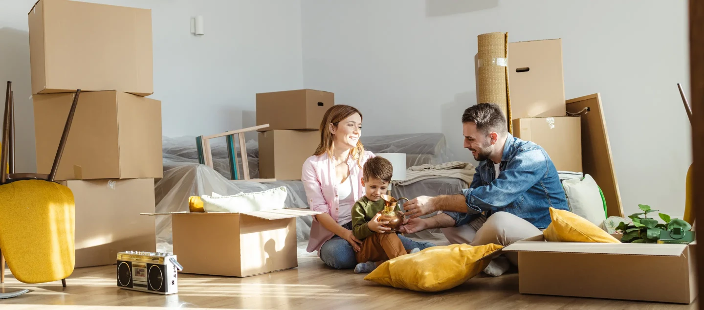 Family sitting on floor of new home surrounded by moving boxes.