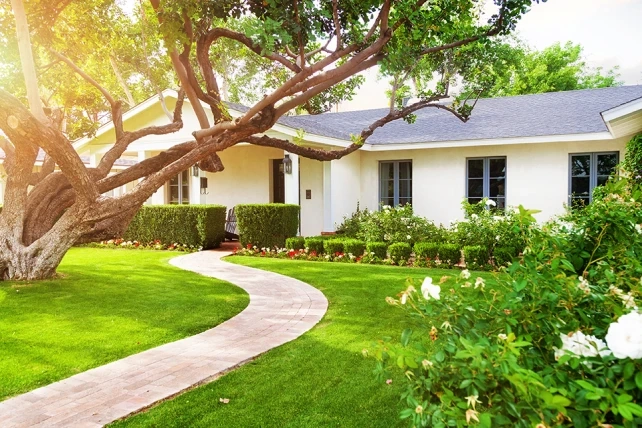 White house with large windows, green lawn, winding path, and colorful flower beds.