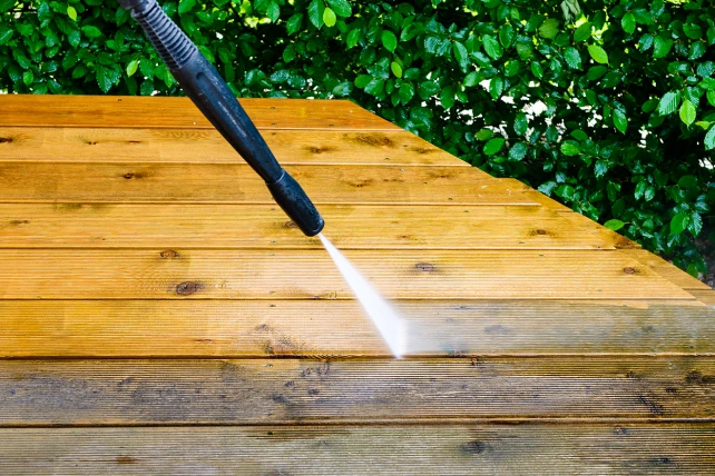 A pressure washer spraying water onto wooden decking.