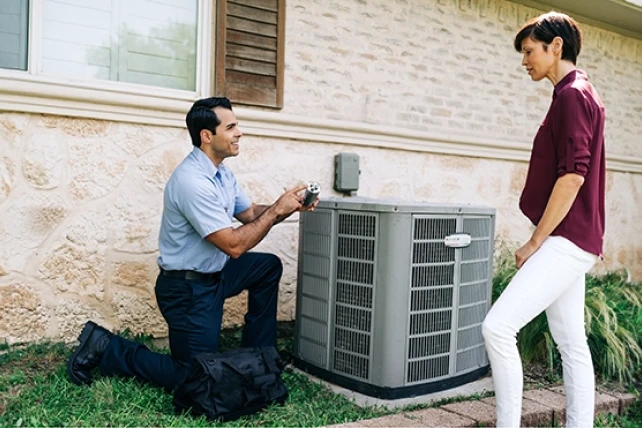Aire Serv tech kneeling beside air conditioning unit speaking with female customer.