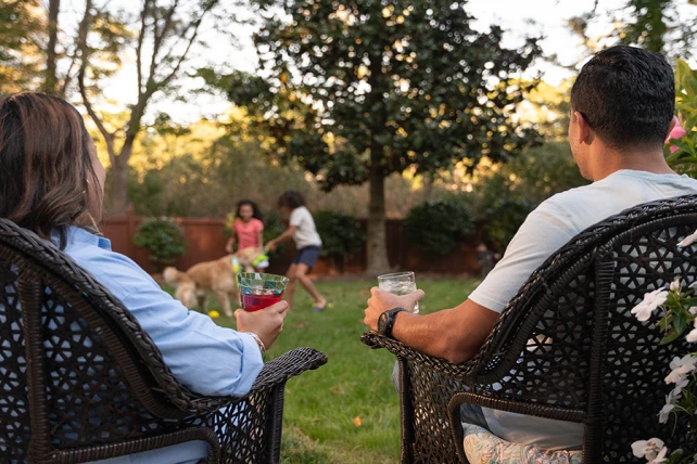 Two people sitting in backyard watching kids play.