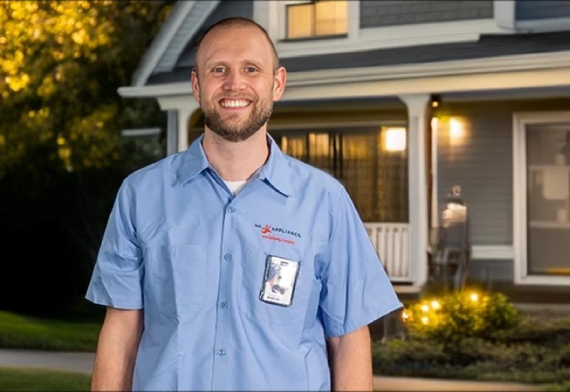 A smiling man in a light blue Mr. Appliance uniform shirt stands outside a house.