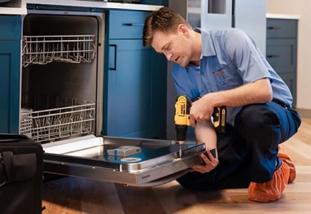 A man is using a power drill to install or repair a dishwasher.