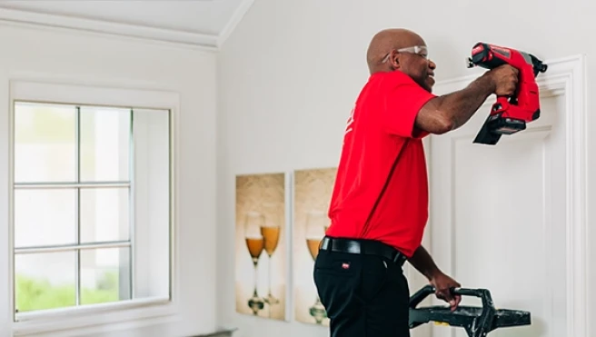 A man using a power drill to install or adjust door trim inside a room.