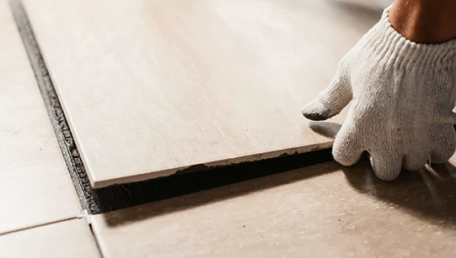 A gloved hand placing a floor tile into position.