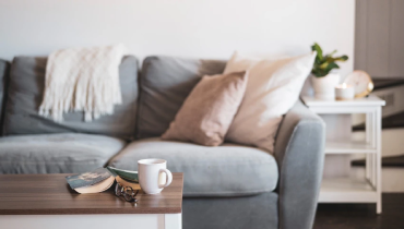 Comfortable gray sofa with pillows and coffee mug on table.