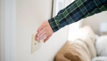 A hand in a plaid shirt reaches for a switch on a wall.