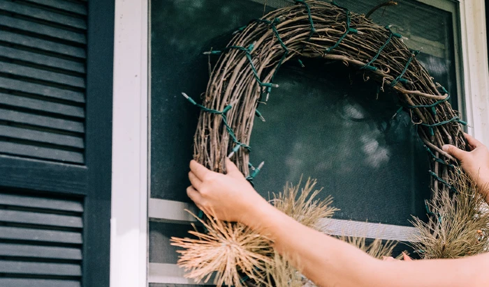 person hanging a wreath on outside of a window on her home