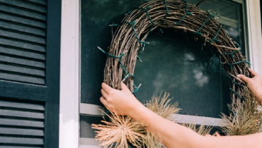 Person hanging a wreath on outside of a window on her home