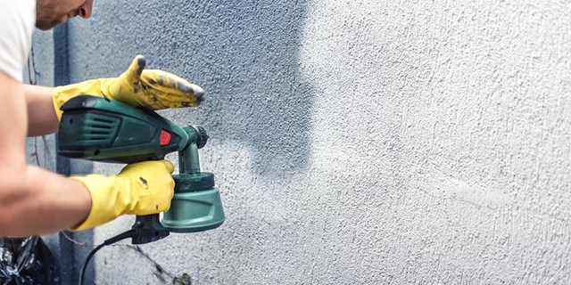 Person using a paint sprayer on the exterior of a home