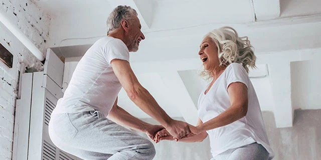 Older couple dressed in white jumping on a bed