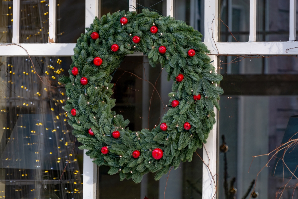 Evergreen wreath with red balls hanging on an exterior window of a home.