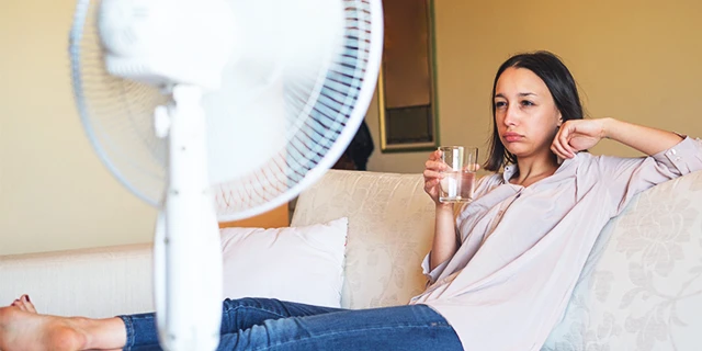 woman frowning with glass of water in front of fan