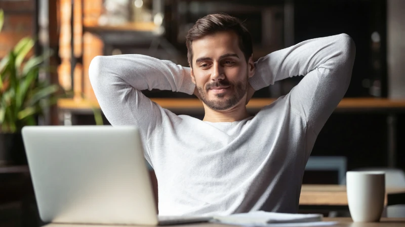 man with hands behind head looking at a laptop