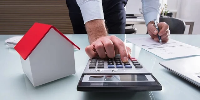 person using calculator next to small home cube