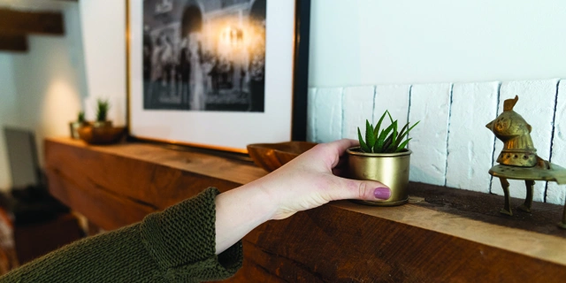 Woman staging a home by adding a plant to the mantel