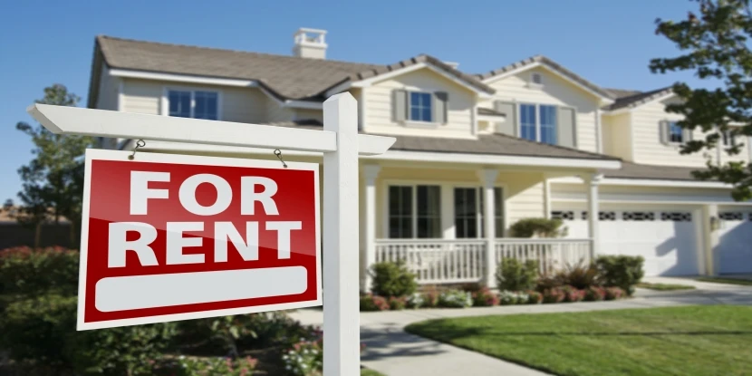 right facing red for rent real estate sign in front of beautiful house.