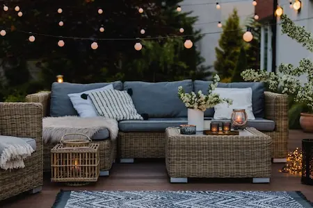 Wicker patio furniture with blue cushions lit by string lights and candles.