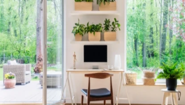 Zen home office with computer and desk in a beautiful, spacious living room interior with plants and view of outside through big windows