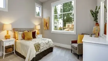Interior of a bedroom with grey walls and carpet, with brown and yellow pillows in a guest house.