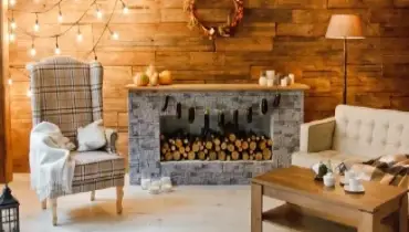 Interior of room with armchair near a fireplace with firewood, wooden wall, wreath and garlands, in a Christmas atmosphere.