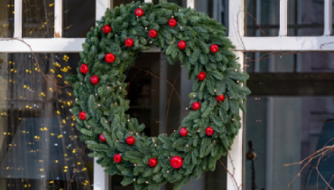 Evergreen wreath with red balls hanging on an exterior window of a home.