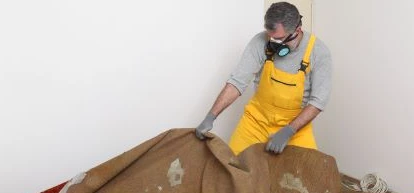 A man in a yellow jumpsuit wearing a respiratory removing carpet from a home.