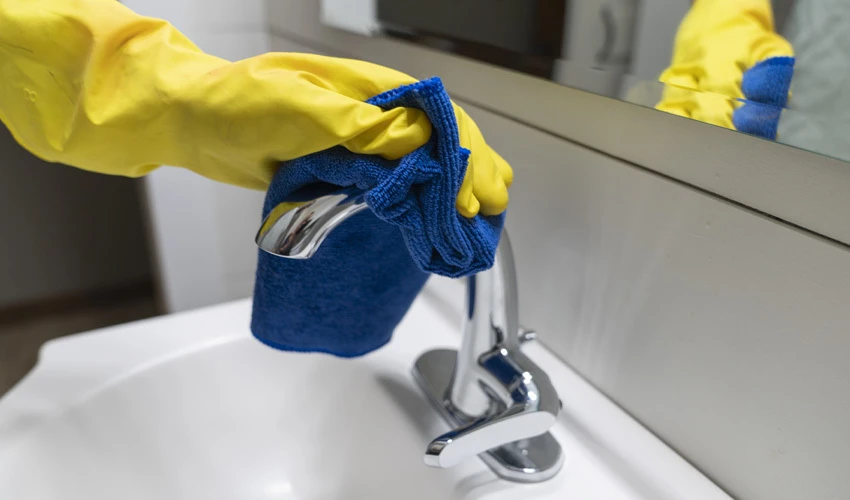 Yellow cleaning glove wiping down chrome faucet.