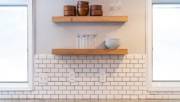 subway tile kitchen backsplash surrounded by two windows and shelves above it.