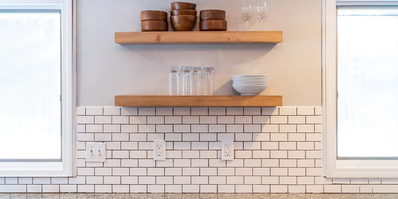 subway tile kitchen backsplash surrounded by two windows and shelves above it.