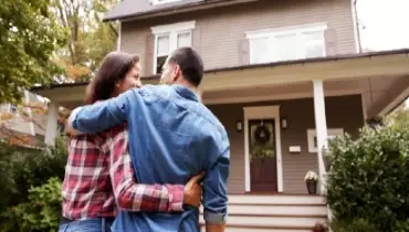 Couple embracing as they stand in front of their new home.
